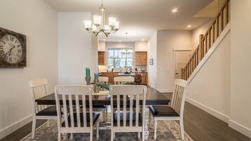 A dining area with a chandelier, a clock, and a staircase leading to another level.