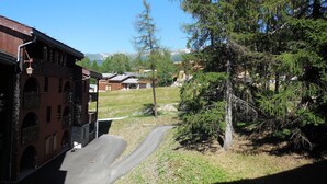 A building with arched windows and a balcony, a paved road, and a grassy area with trees.