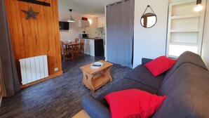 A compact living space with a sofa, a small wooden table, a dining area, and a kitchen.