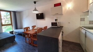 A compact kitchen with a dining area, a TV mounted on the wall, and a coffee machine.