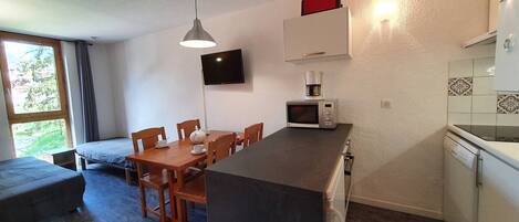 Une cuisine compacte avec un coin repas, un téléviseur fixé au mur et une machine à café.