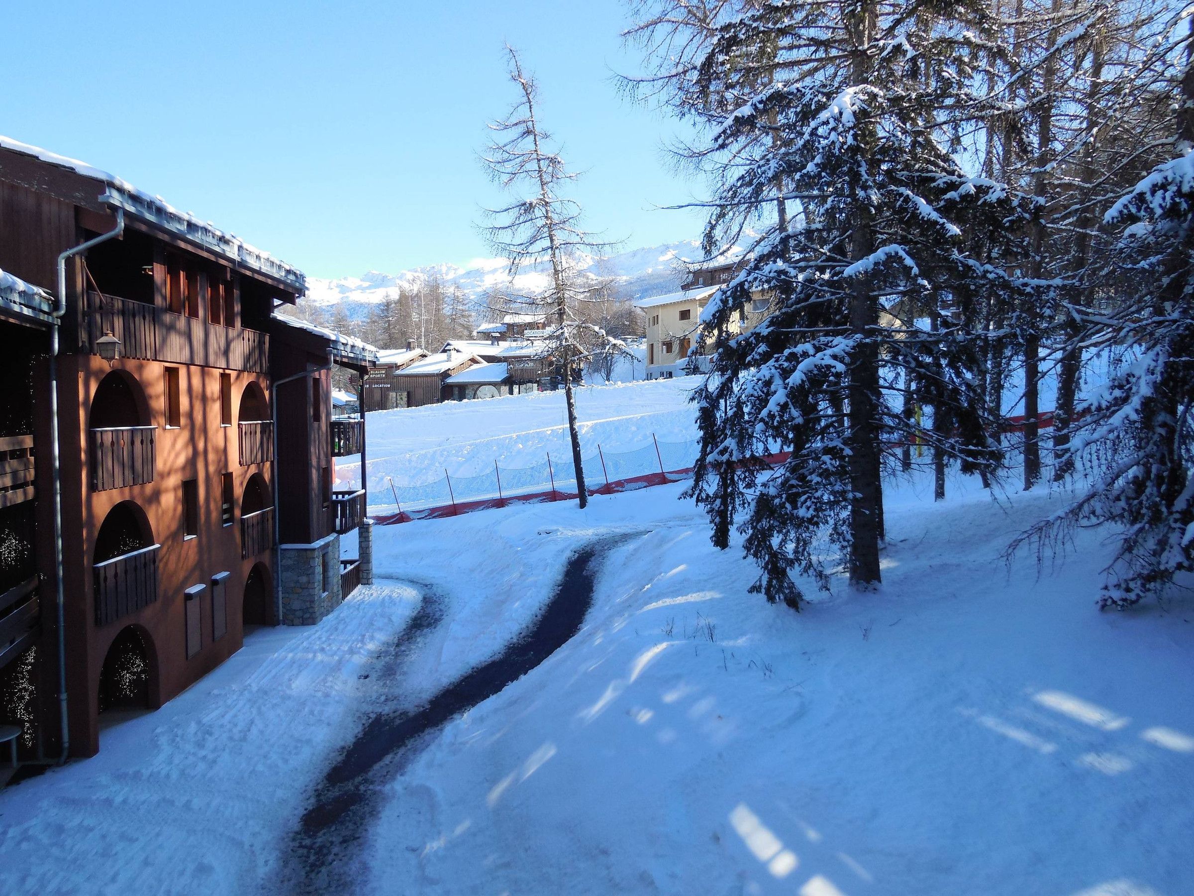 A snow-covered path leading to a building with arched windows and a wooden facade.
