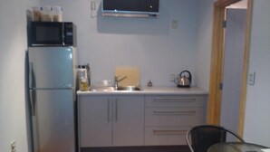A compact kitchen with a refrigerator, microwave, and a small table with a chair. - Luxury Self Contained Unit,Wide Views (Portage)