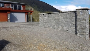 A modern building with a garage, a stone wall, and a mountainous backdrop. - Luxury Self Contained Unit,Wide Views (Portage)