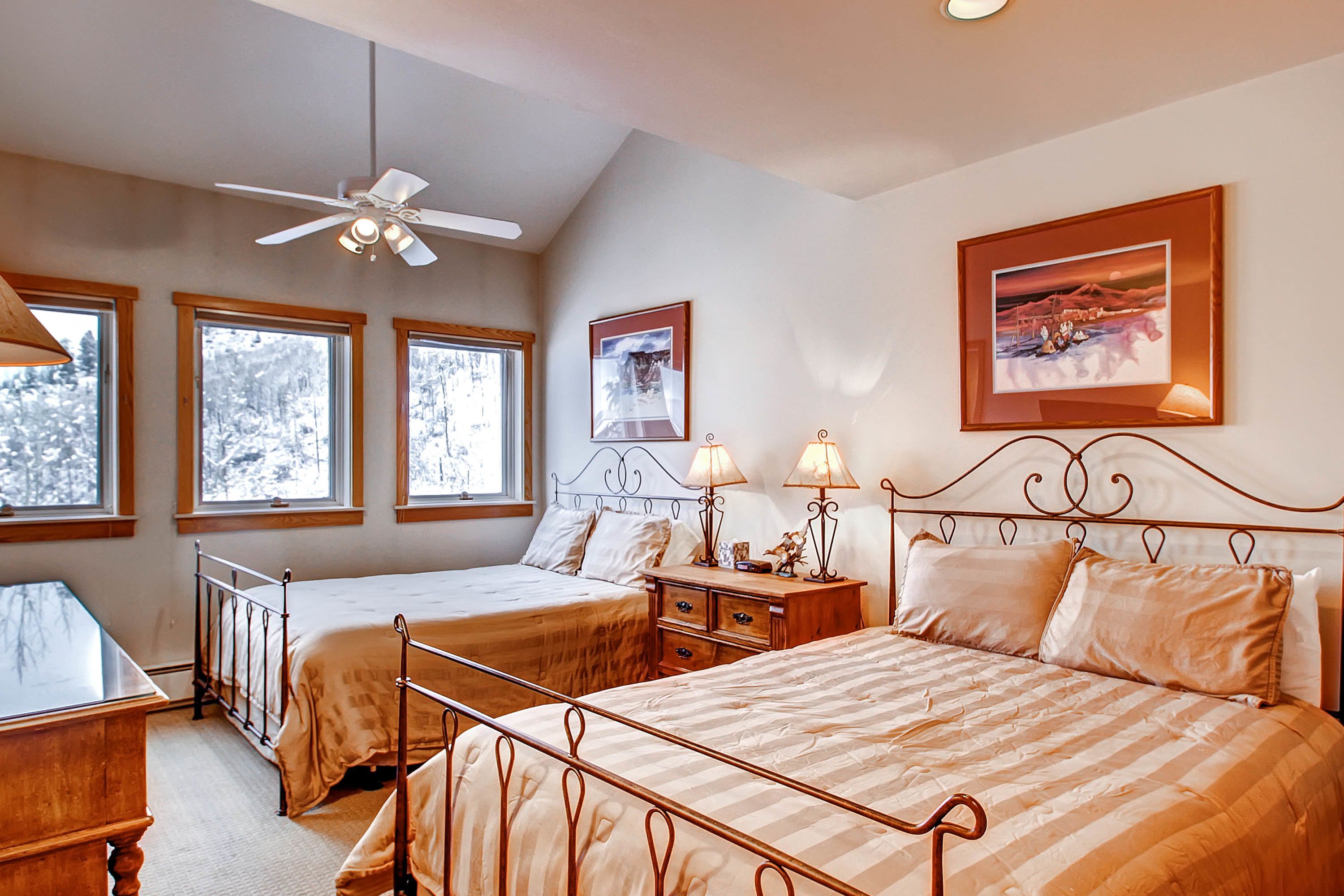 A bedroom with two beds, a ceiling fan, and a large window with a view of trees.