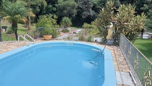 Una piscina con solárium de piedra, rodeada de plantas en macetas y una estatua.