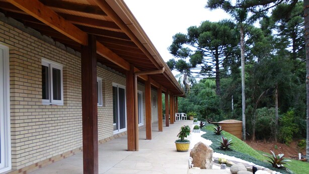 Un espacio al aire libre techado con un edificio de ladrillo, un sendero de piedra, columnas de madera y plantas en macetas.