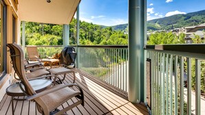A wooden deck with outdoor seating, a grill, and a view of a forested hillside. - Centennial 4 Bedroom Condo Unit no. 29 (Avon)