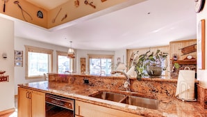 A kitchen with a granite countertop, stainless steel sink, wooden cabinets, and a dishwasher. - Centennial 2 Bedroom Condo Unit no. 10 (Avon)