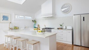 A modern kitchen with white cabinetry, a central island with stools, a stainless steel refrigerator, and a wall clock.