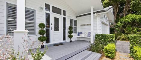 A white house with a porch, a bench, and a small garden.