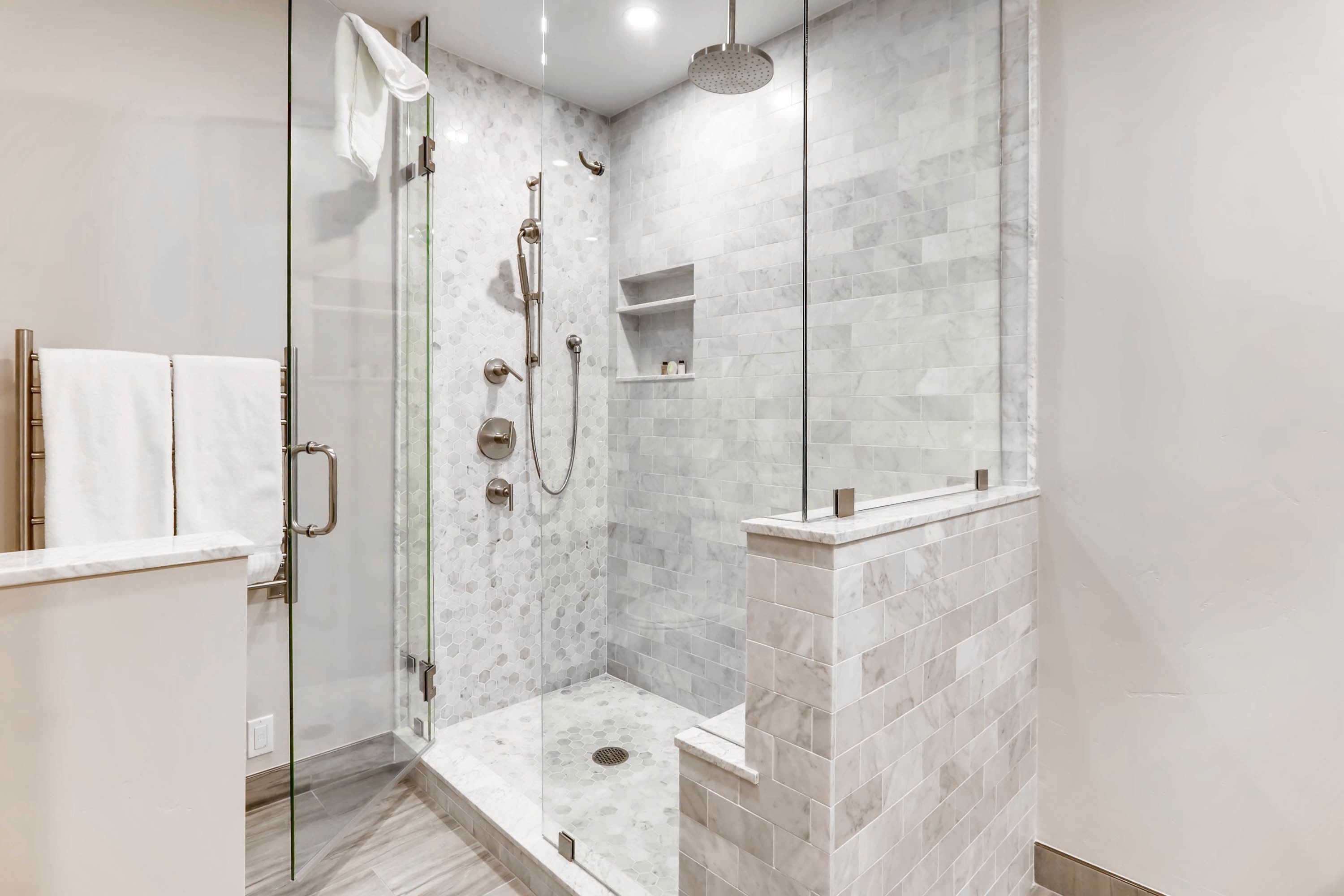 A modern shower with a glass door, a handheld showerhead, and a wall-mounted faucet.