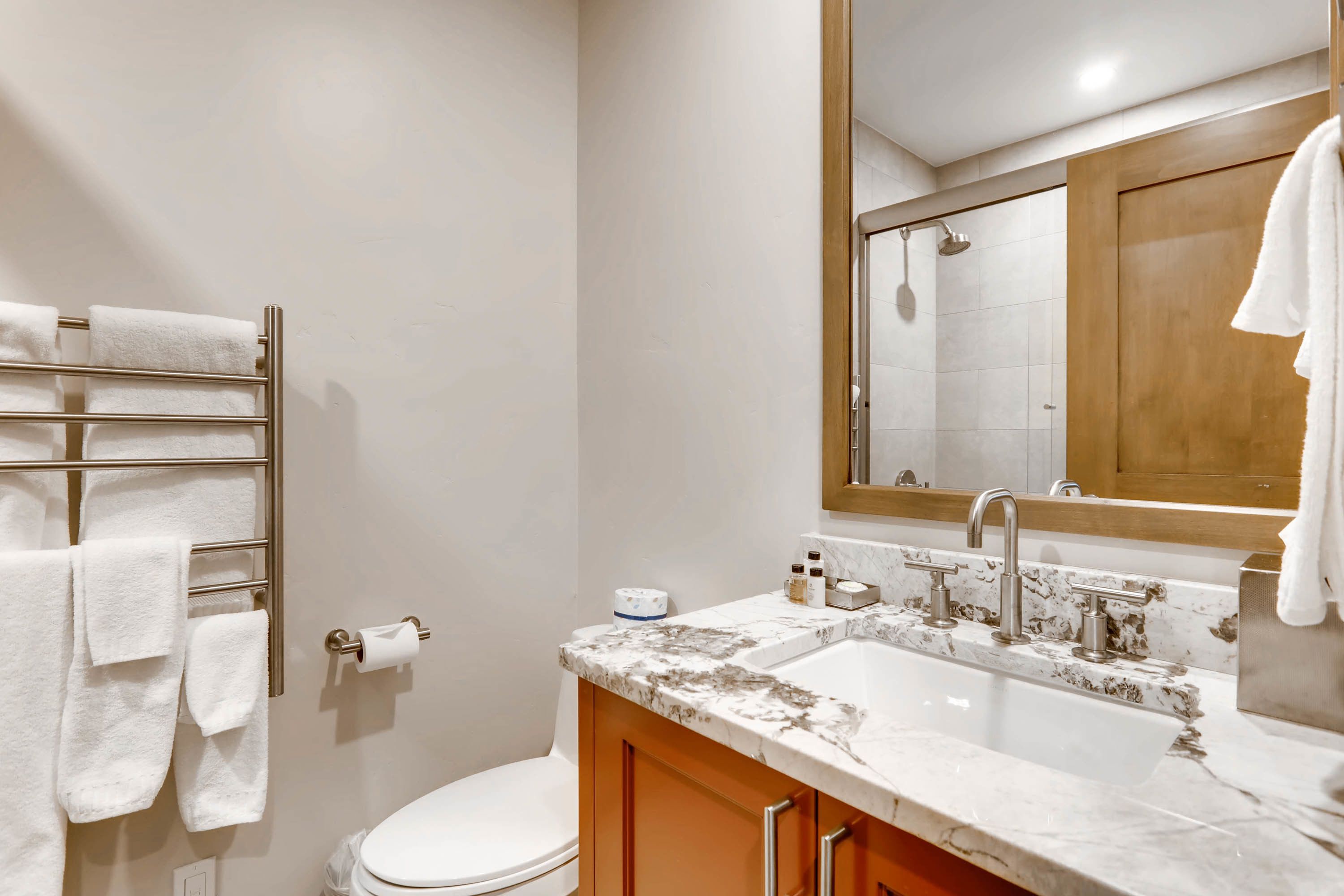 Un baño con lavamanos de mármol, toallero, inodoro y espejo.