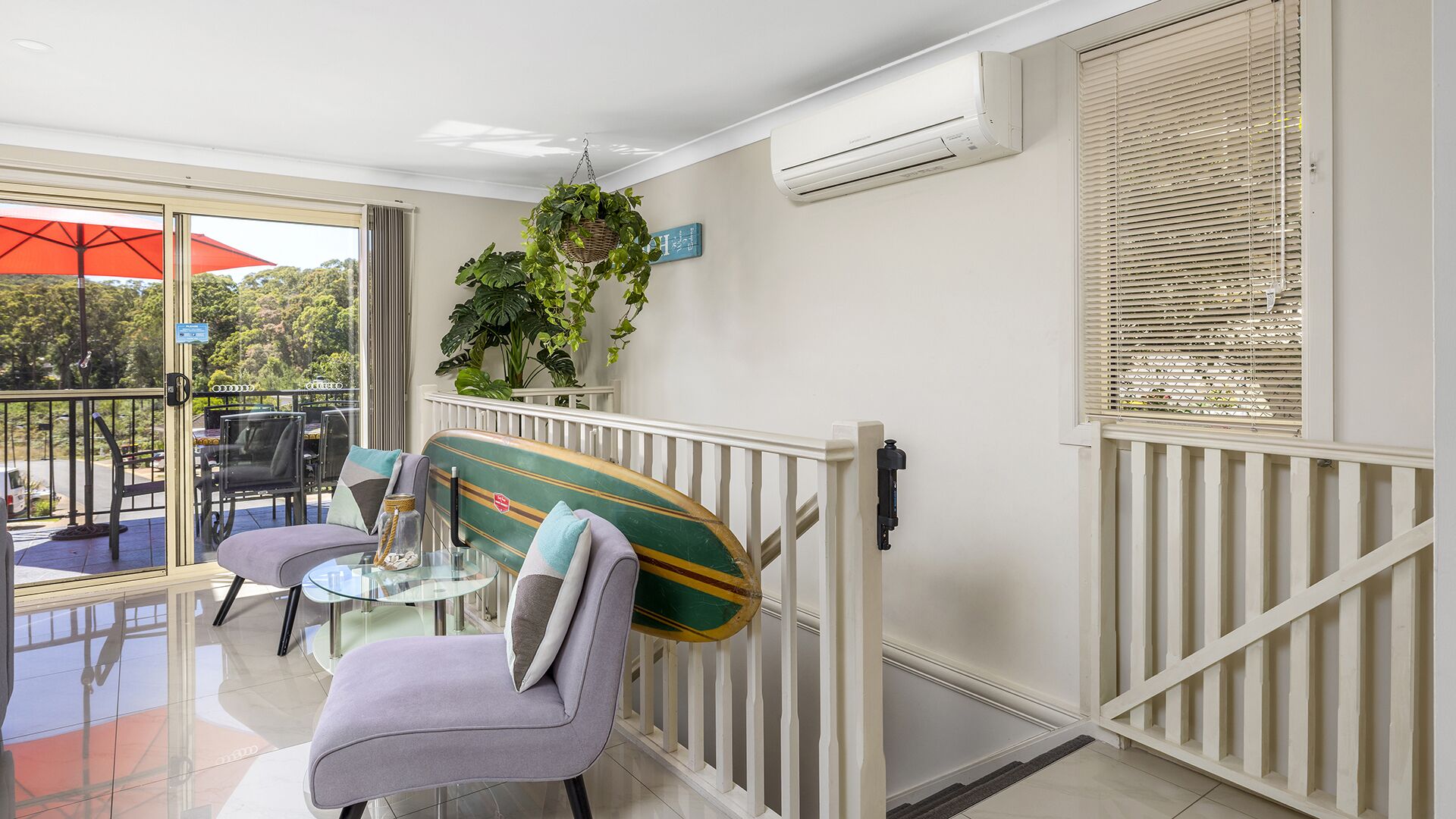 Een balkon met een glazen tafel, stoelen en een surfplank tegen de reling geleund.