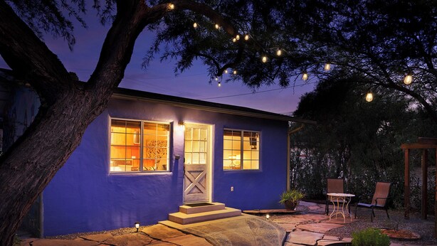 A house with a blue exterior, a stone pathway leading to the entrance, and outdoor seating with chairs and a table.