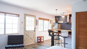 A compact room with a sofa, a small table, a bar area with stools, and a door with a window.