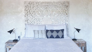 A bed with a patterned bedspread and pillows, flanked by two nightstands with lamps and a decorative wall panel above.