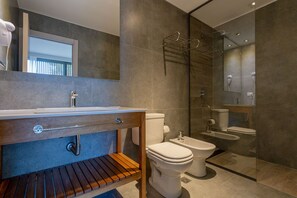 A modern bathroom with a wooden vanity, a toilet, a bidet, and a glass shower enclosure. - Destinar Apart Hotel (Carilo)