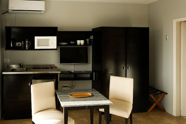A compact kitchen with a microwave, coffee maker, and a flat-screen TV. There are two chairs and a small table with a tray. - Destinar Apart Hotel (Carilo)