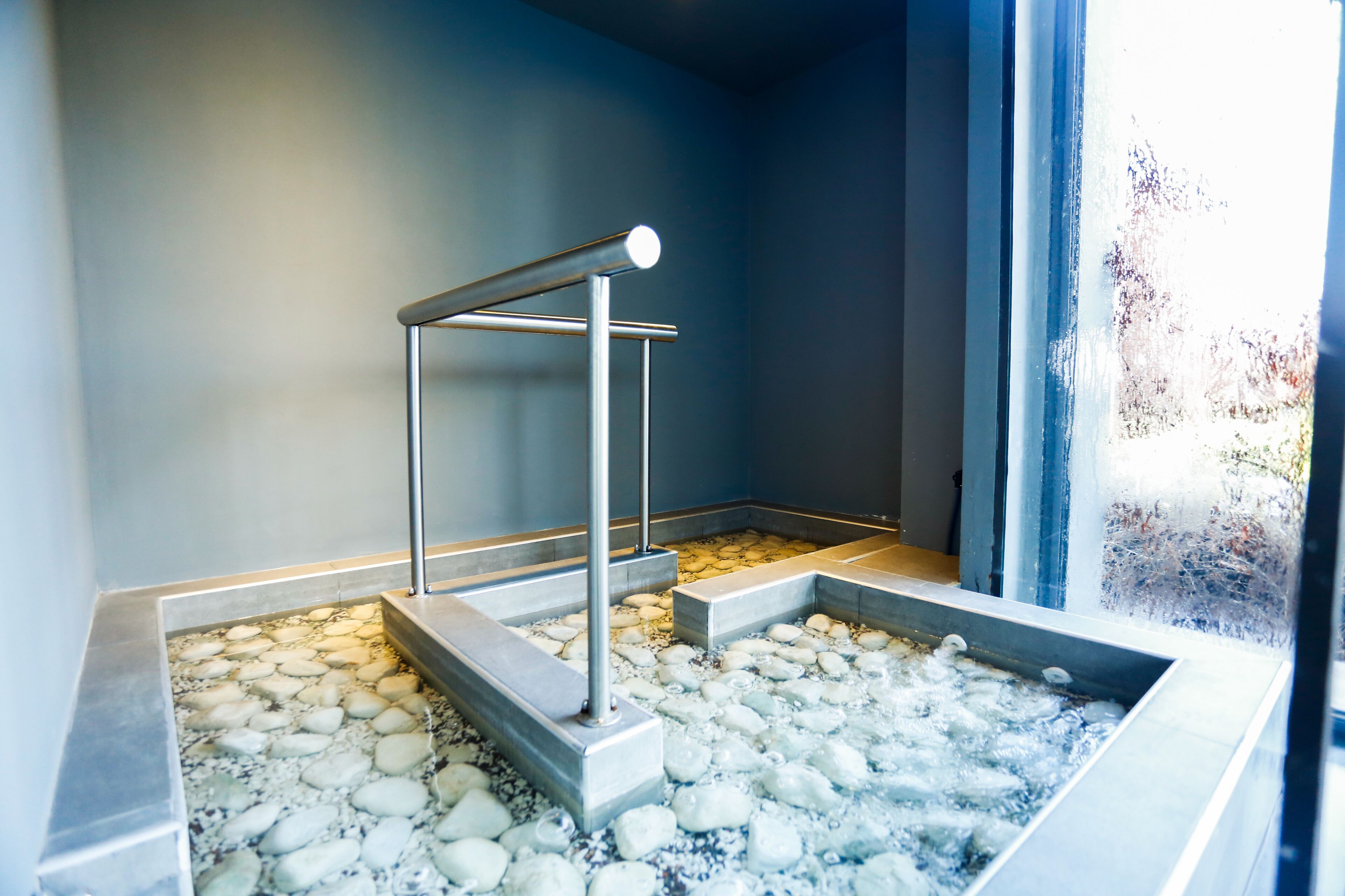 A spa area with a stone floor, a metal bench, and a view of the outdoors through a window.
