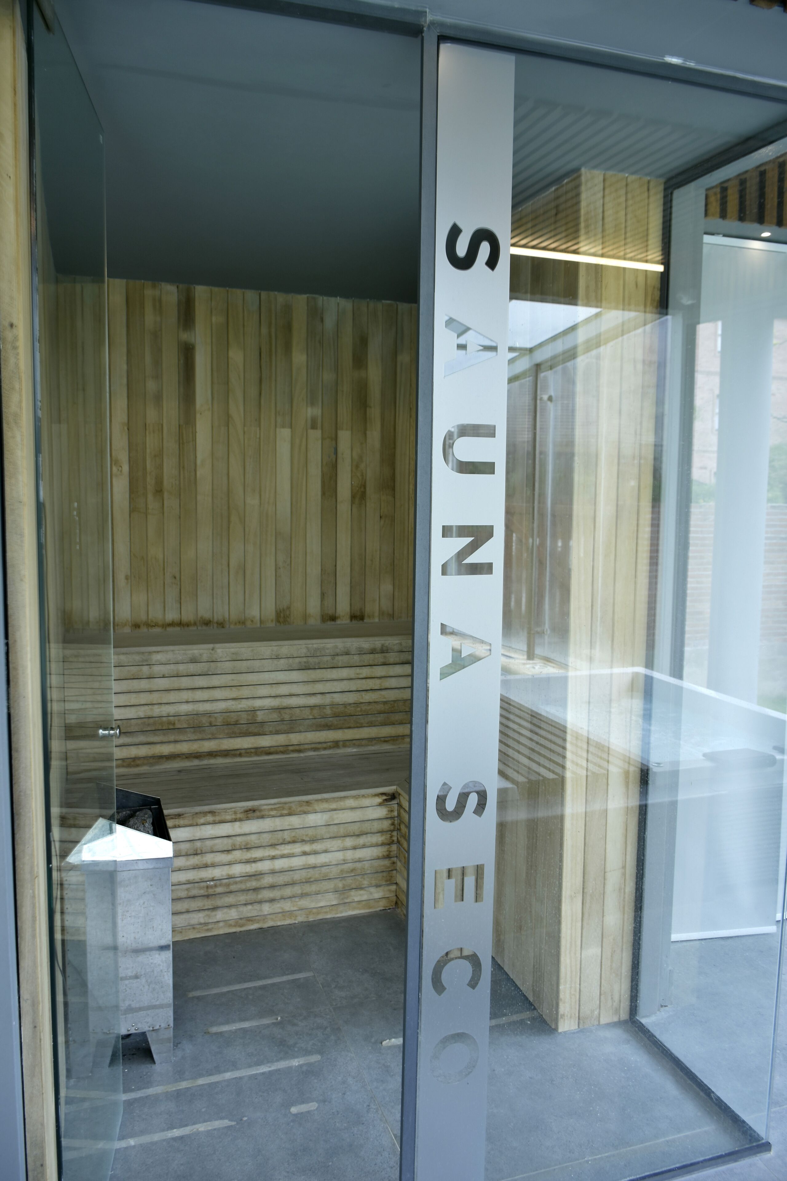 A sauna room with wooden walls and a glass door.