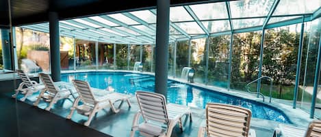A swimming pool with lounge chairs and a glass ceiling.