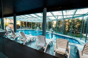 Una piscina con sillones de descanso y techo de vidrio.
