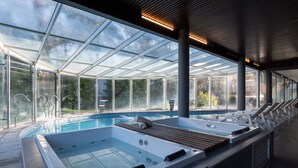 A modern indoor swimming pool with glass walls, a wooden deck, and a hot tub. - Destinar Apart Hotel (Carilo)