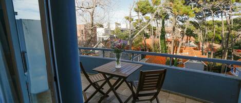 A balcony with a table and chairs, overlooking a residential area with trees and buildings.
