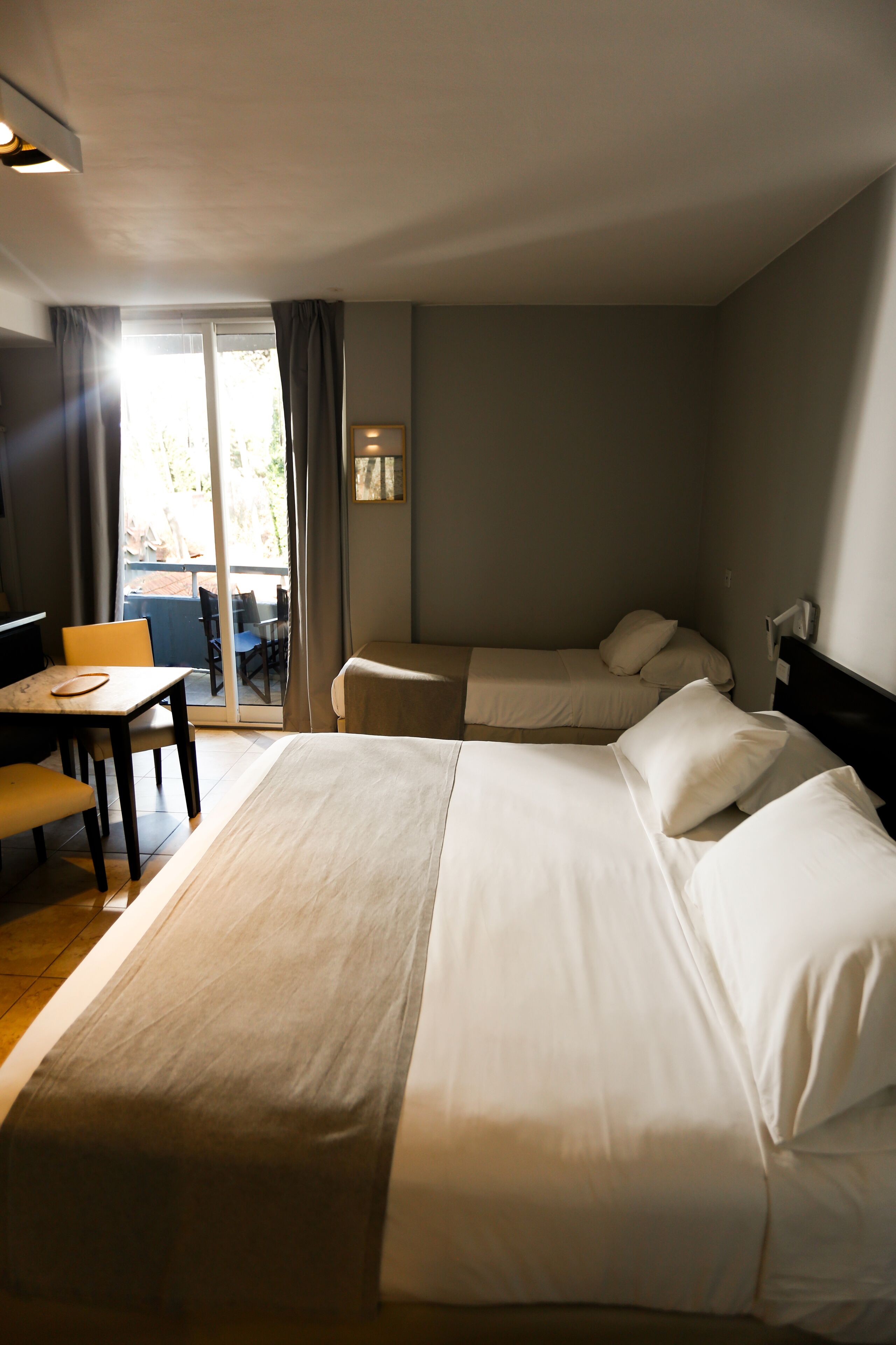Habitación de hotel con una cama grande, un escritorio y una silla. Posee una puerta corredera que da a un espacio exterior.