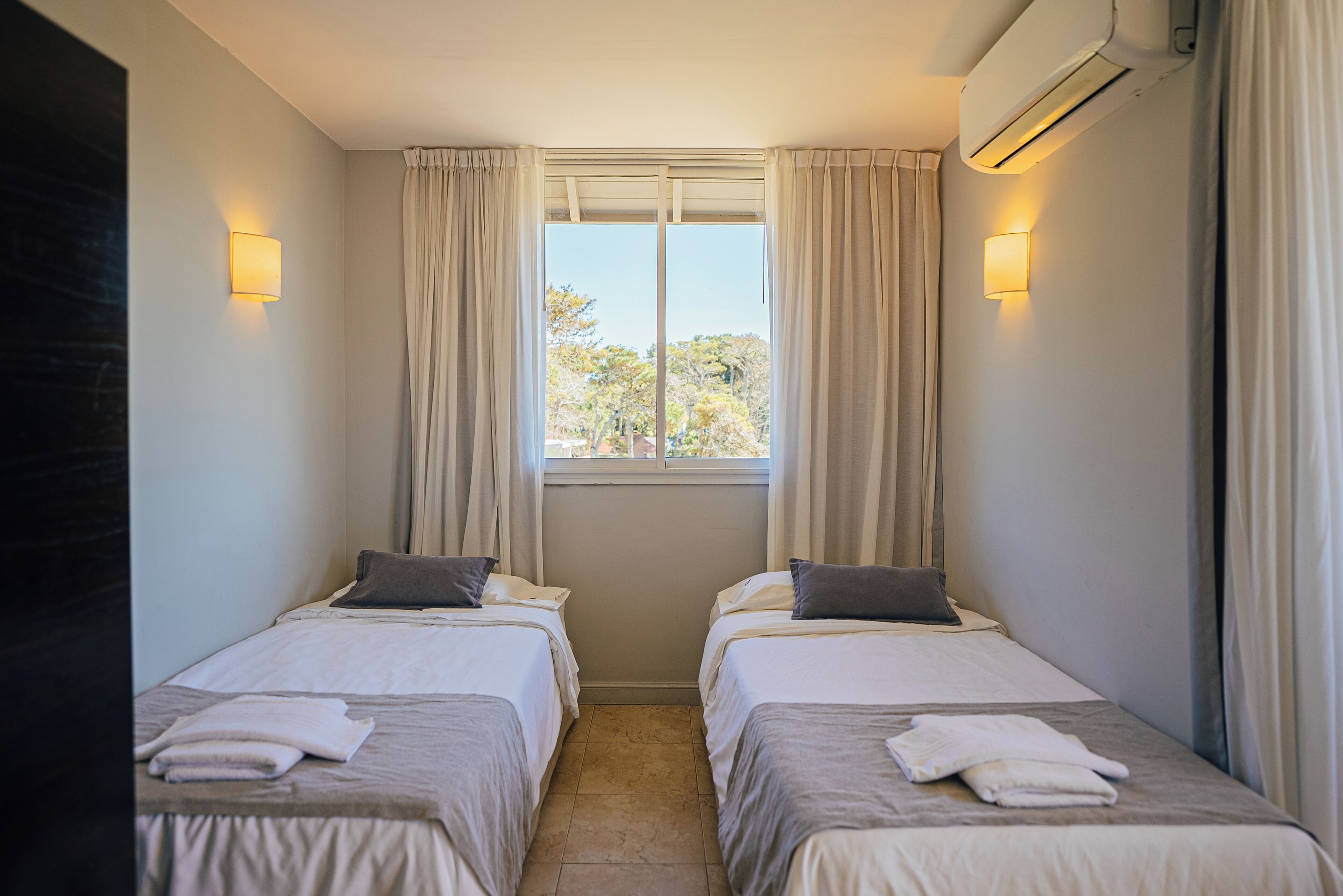 Habitación doble con dos camas, una ventana con cortinas e iluminación en la pared.