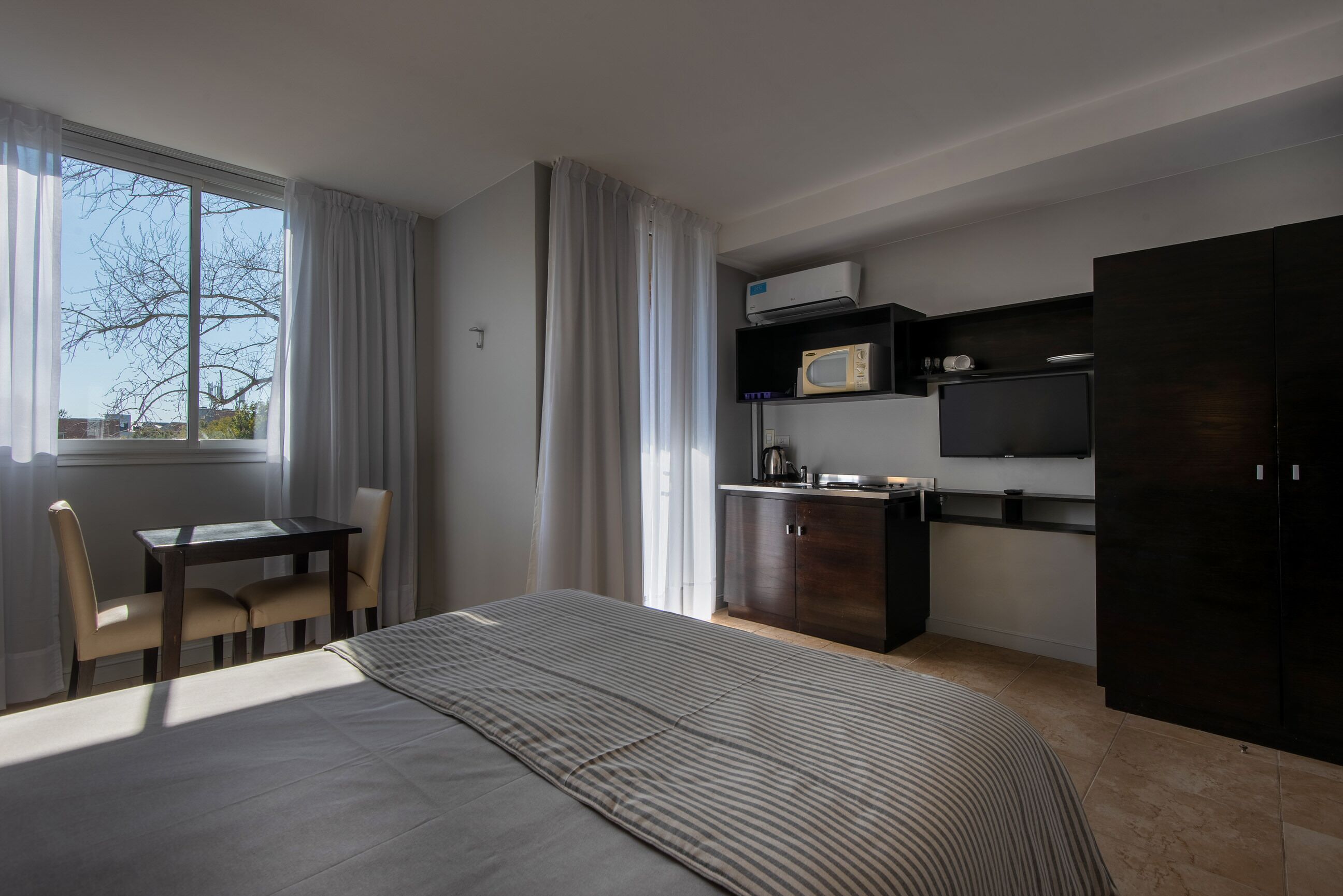 A modern hotel room with a bed, a desk, a chair, a TV, a microwave, and a wardrobe.