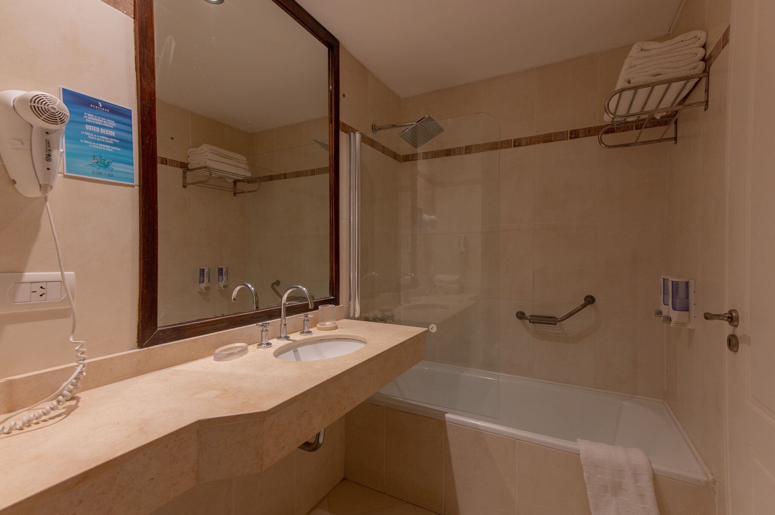 Ein Badezimmer mit Waschbecken, Spiegel und Dusche. An der Wand befinden sich ein Handtuchhalter und ein Föhn.