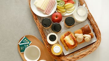 Bandeja de desayuno con jamón, queso, frutas, yogur y pastelería sobre un tapete tejido.