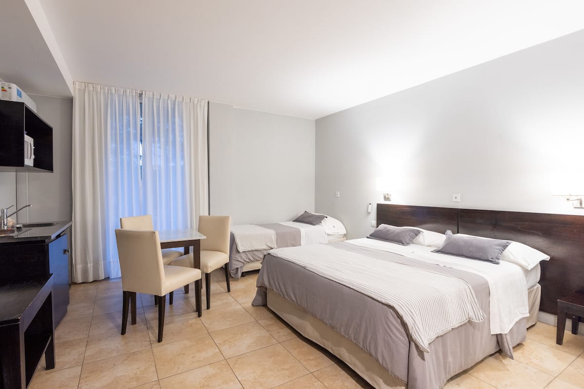 A hotel room with a bed, a desk, a chair, a TV, and a window with curtains.