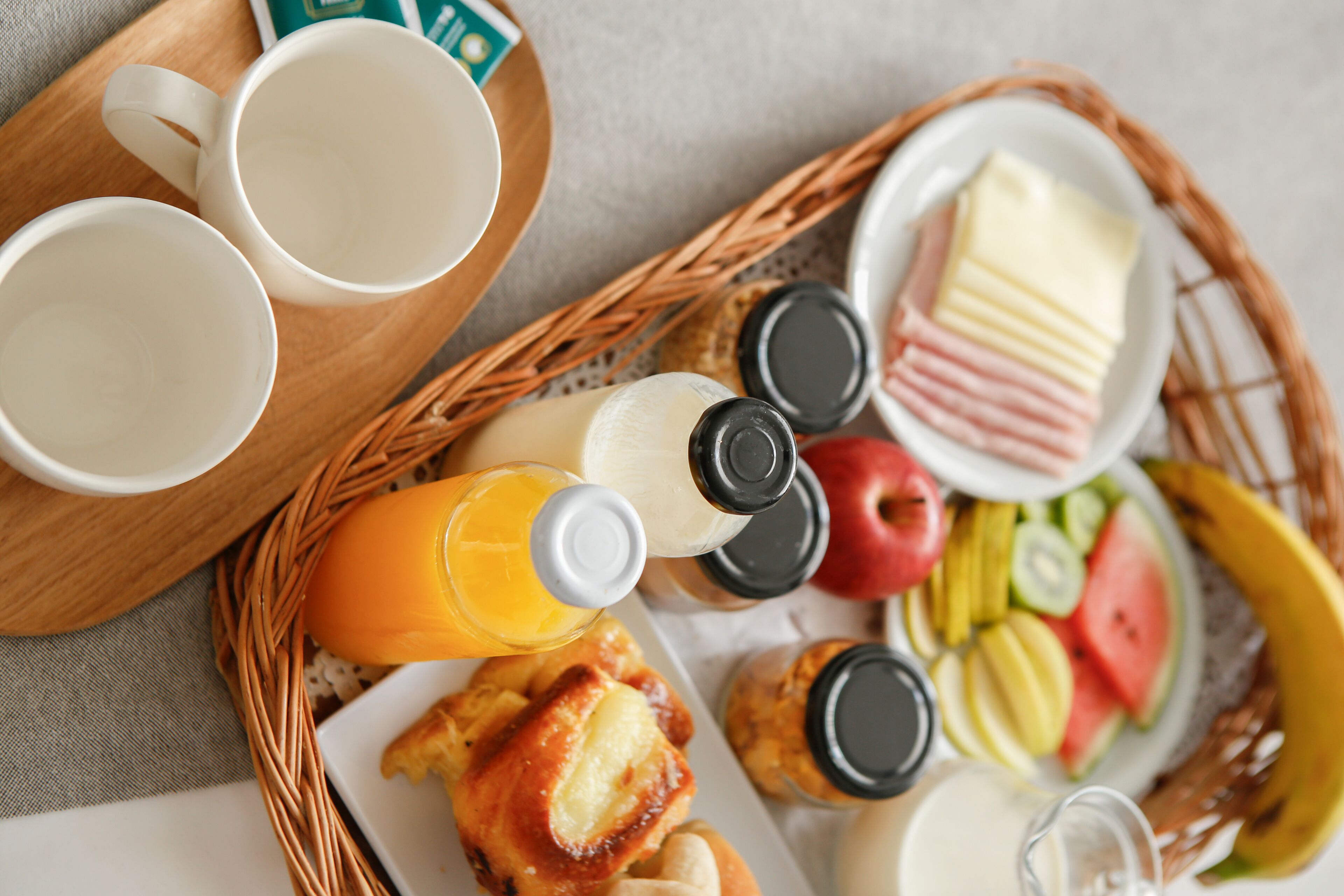 A breakfast tray with coffee cups, orange juice, butter, jam, cheese, ham, eggs, and fruit.