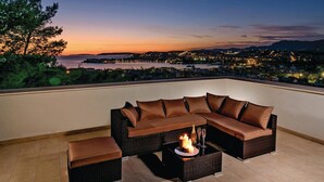 A sectional sofa with a fire feature on a rooftop terrace with a city view.