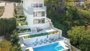 A modern two-story house with a swimming pool, outdoor seating, and a lush garden.