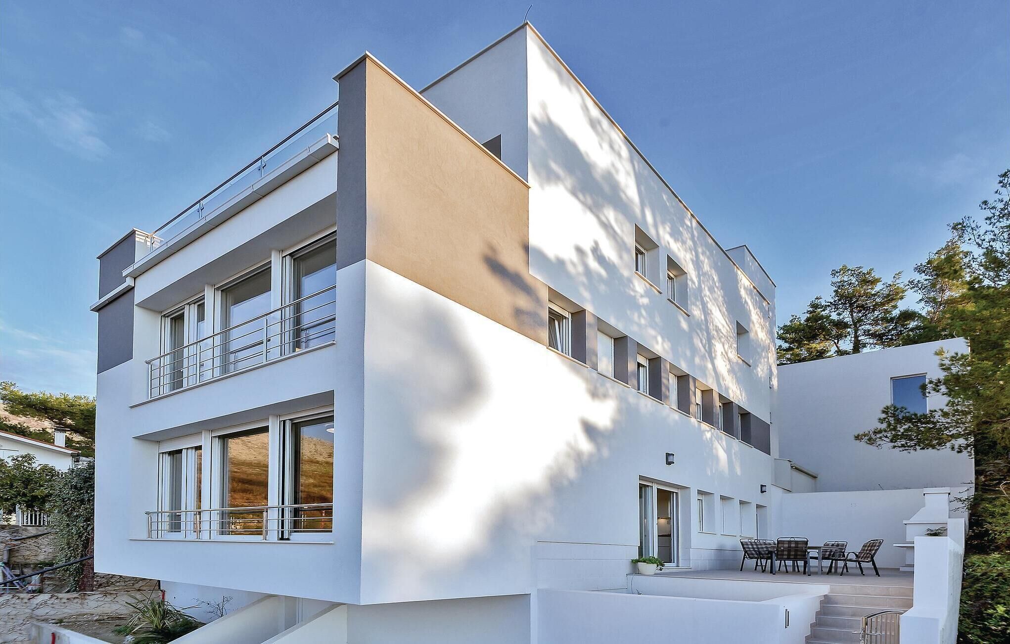 Un edificio moderno a due piani con ampie finestre, un balcone e un patio con posti a sedere all'aperto.