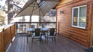Una terraza de madera con una mesa, sillas y un paraguas grande, además de una ventana.