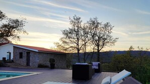 Ein Poolbereich mit Liegestühlen, ein Steinhaus und eine Landschaftsansicht.