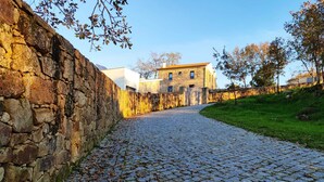 Ein Kopfsteinpflasterweg führt zu einer Steinmauer und einem Gebäude mit einem Ziegeldach.