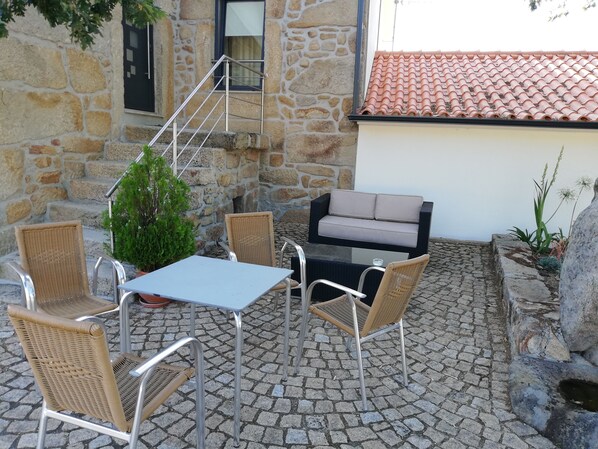 Un patio al aire libre con paredes de piedra, una mesa de vidrio, sillas de mimbre, un sofá y una planta pequeña.