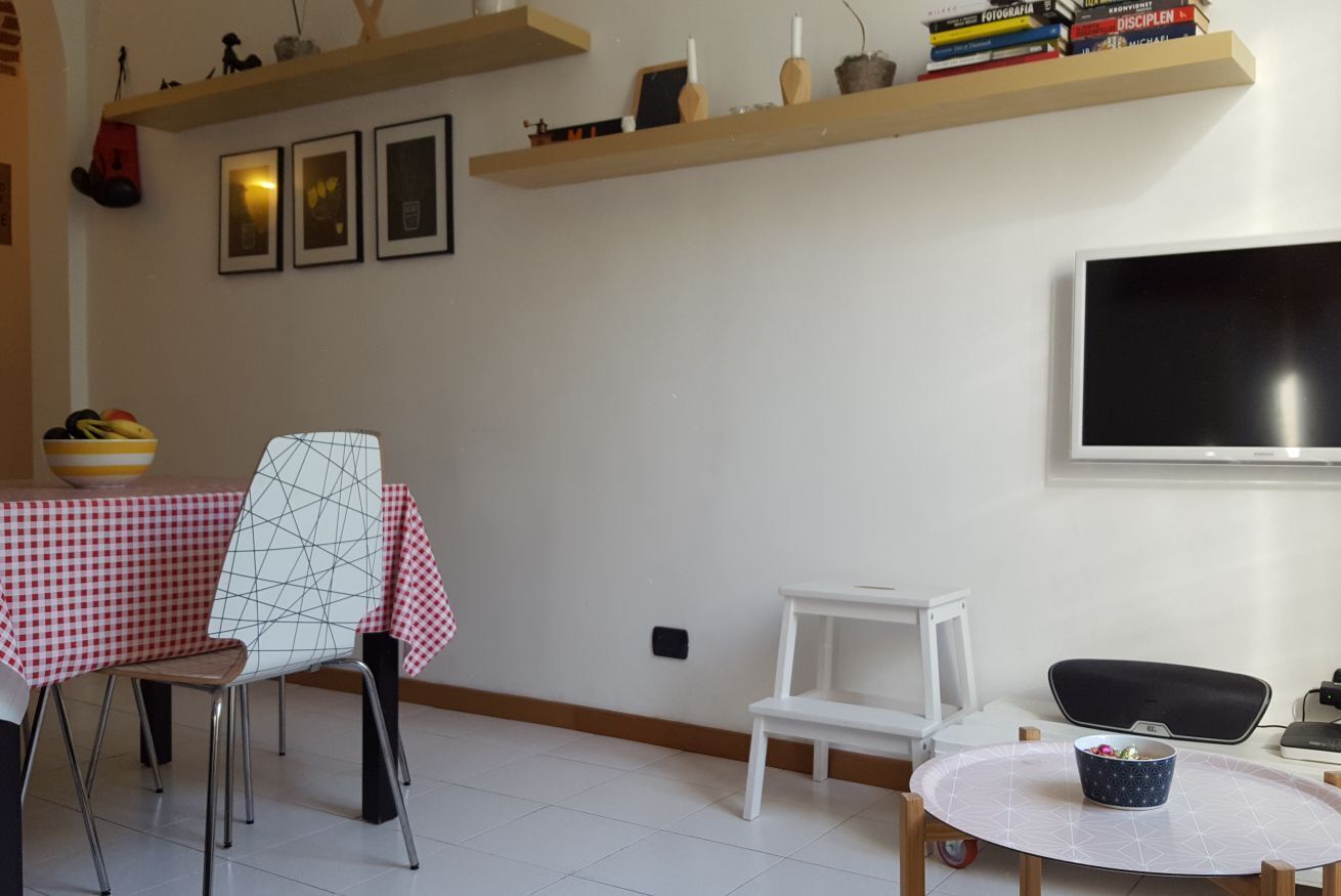 Un coin repas avec une nappe à carreaux, une chaise à motifs géométriques, une chaise blanche, une petite table blanche et un bol posé sur une table ronde.