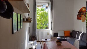 A modern living room with a sofa, a dining table with a checkered tablecloth, and a window with curtains.