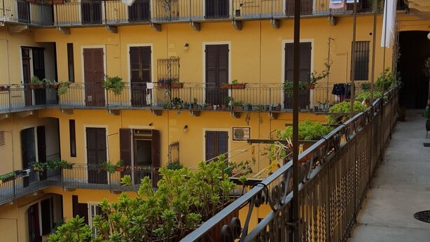 A multi-story yellow building with balconies, some with plants.