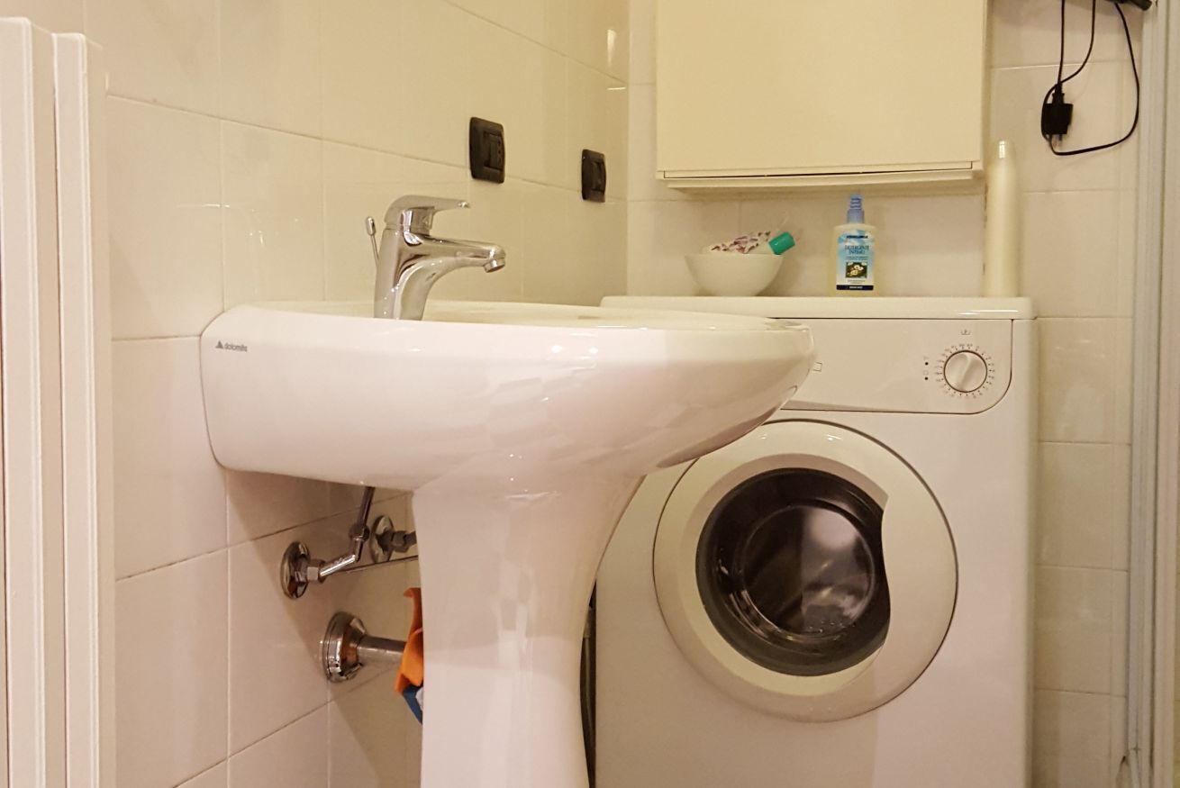 A bathroom with a sink, a washing machine, and a cabinet above the machine.