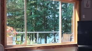 Una habitación con un ventanal grande, vigas de madera, un estante blanco, un televisor y un calentador.