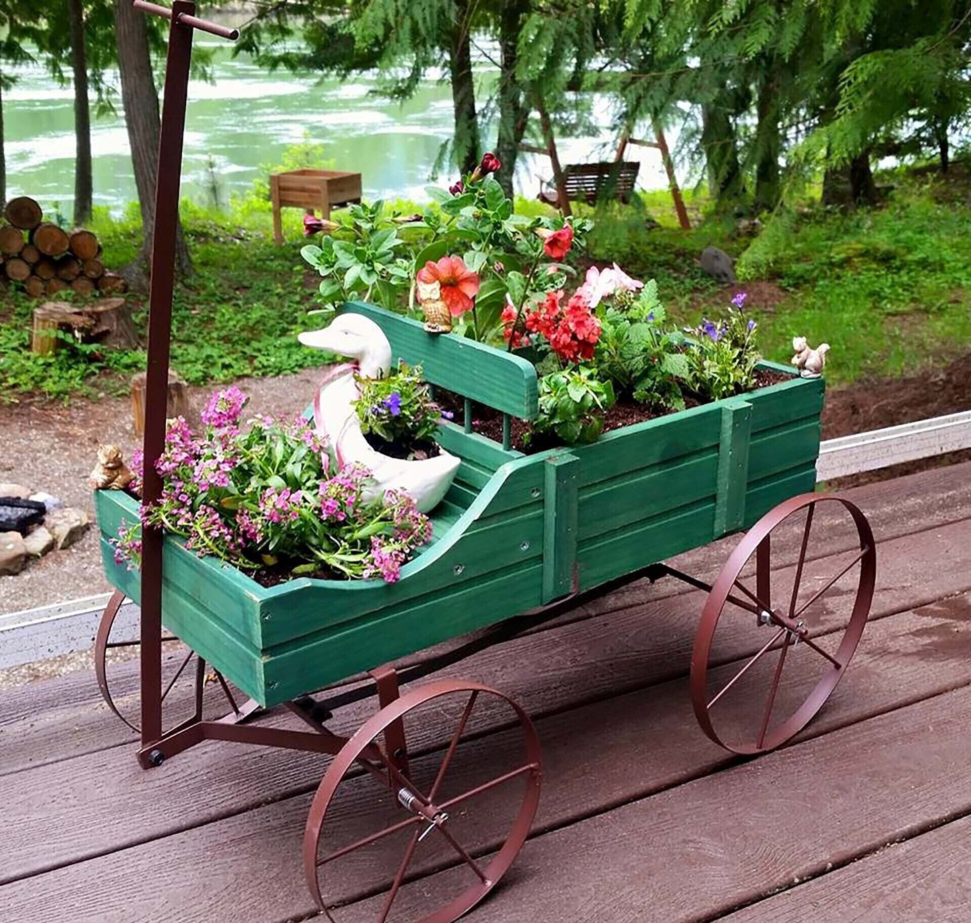 A green wooden cart with flowers and a duck decoration, placed on a wooden deck.