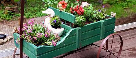 A green wooden cart with flowers and a duck decoration, placed on a wooden deck.